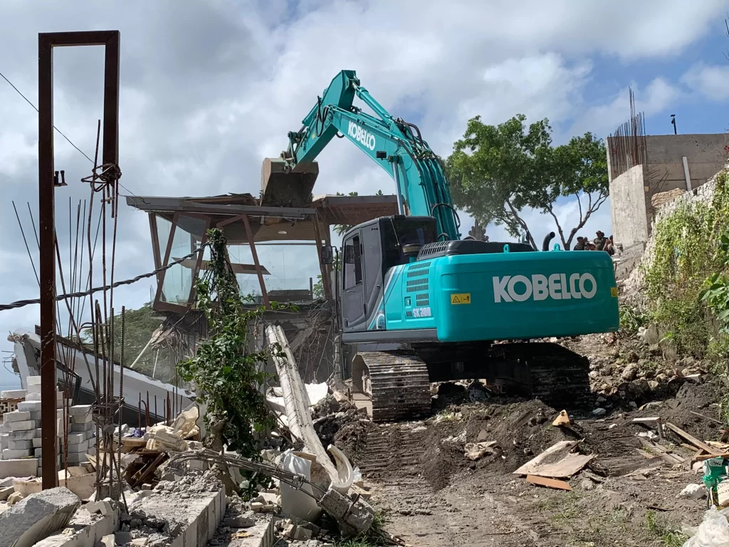 Excavator demolishing an illegal building in Bali during zoning enforcement operation, Bingin Beach, July 2025