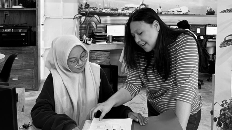 Magie Moretha, Compliance Manager at TraceWorthy, guiding an intern through a printed policy document during a training session in the Bali office.