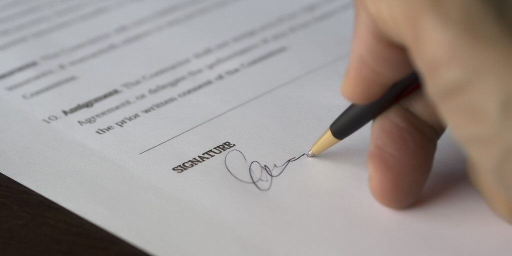 Hand signing a document above a signature line